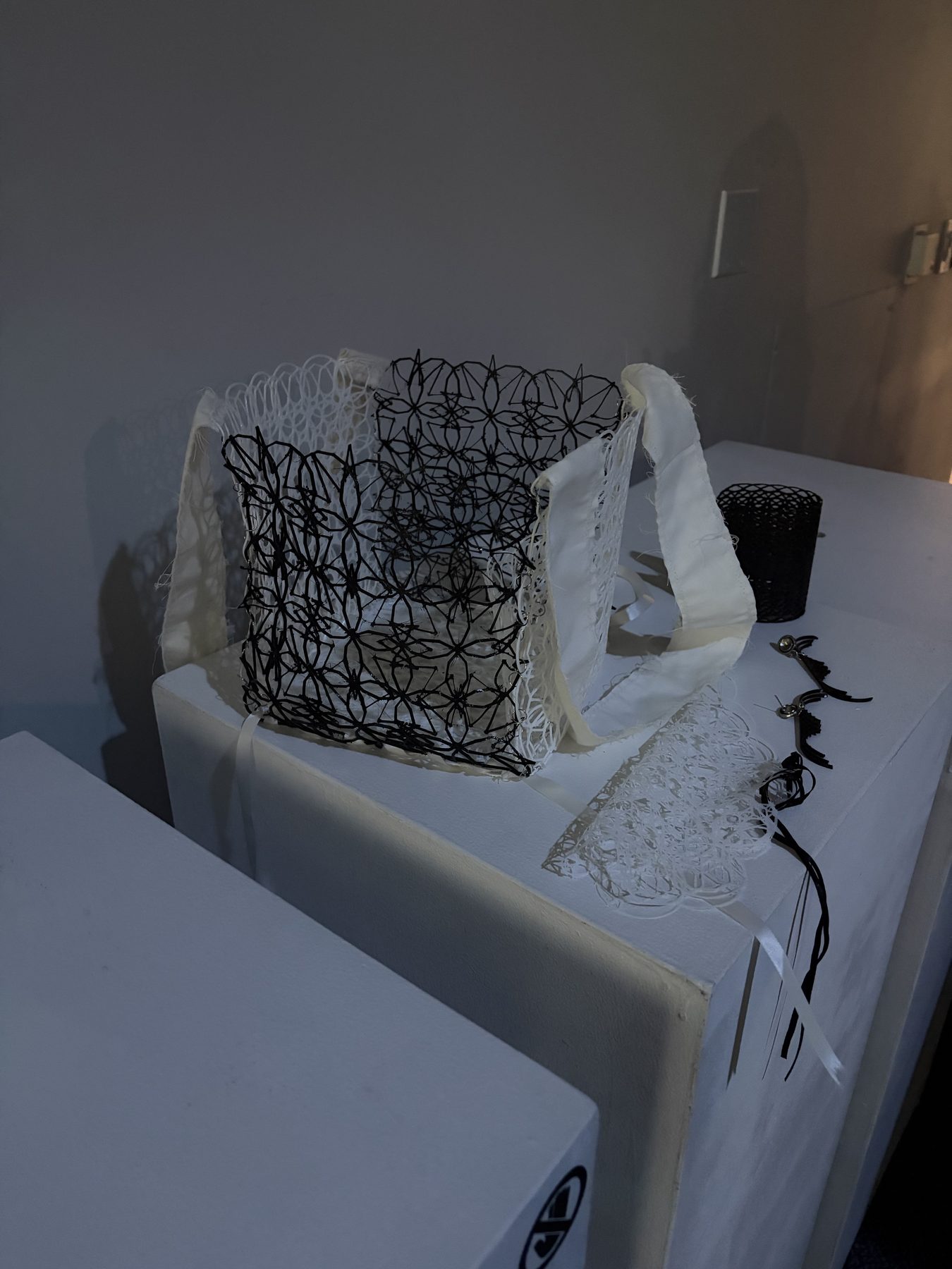 Eternal Purse with black and white 3D-printed lace panels and fabric straps, full view, next to additional 3D-printed accessories